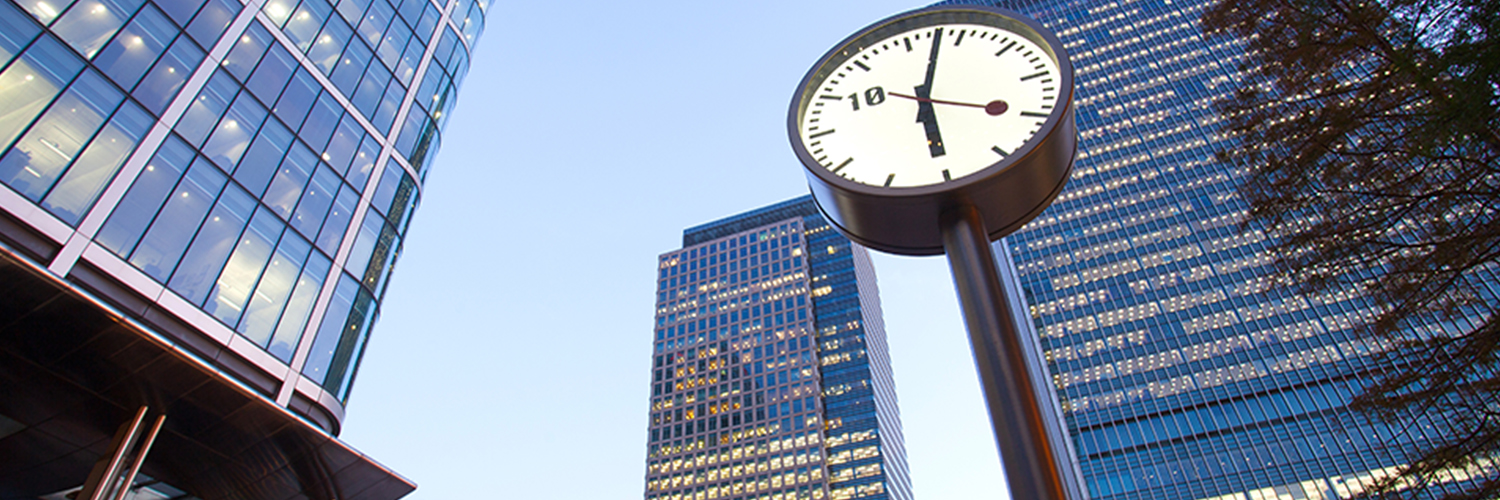 A clock outside some skyscrapers in London